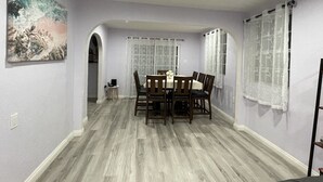 A dining area with a round table and chairs, a painting on the wall, and a window with curtains. - Entire Newly Renovated House in North Pomona (Pomona)
