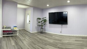 A room with a flat-screen TV mounted on the wall, a potted plant, and a shoe rack with shoes and a small table with items. - Entire Newly Renovated House in North Pomona (Pomona)
