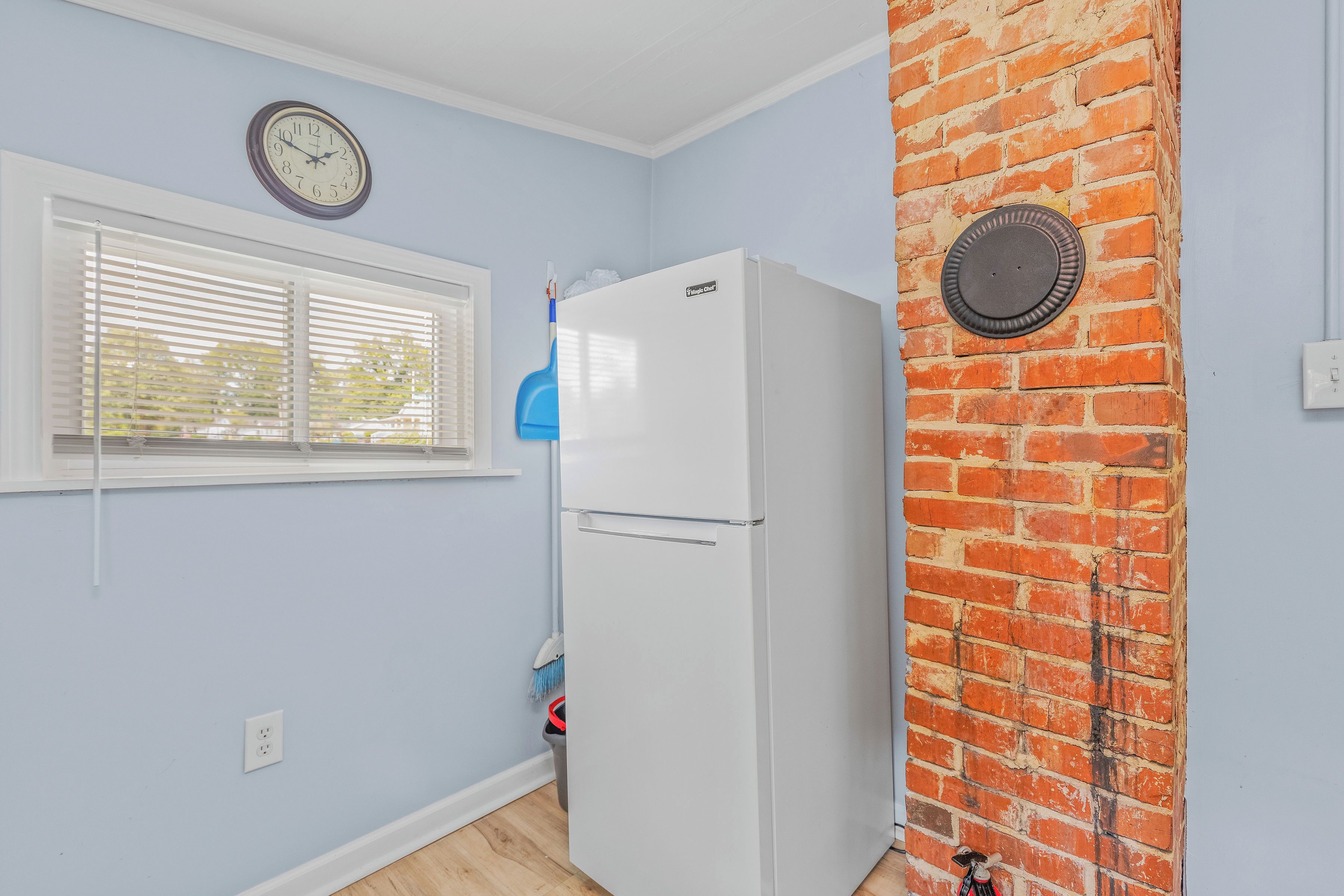 Una cocina con un refrigerador blanco, un reloj en la pared y una ventana con persianas.