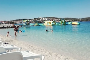 Una spiaggia con acque cristalline, un litorale ciottoloso e strutture gonfiabili per divertimento in acqua.