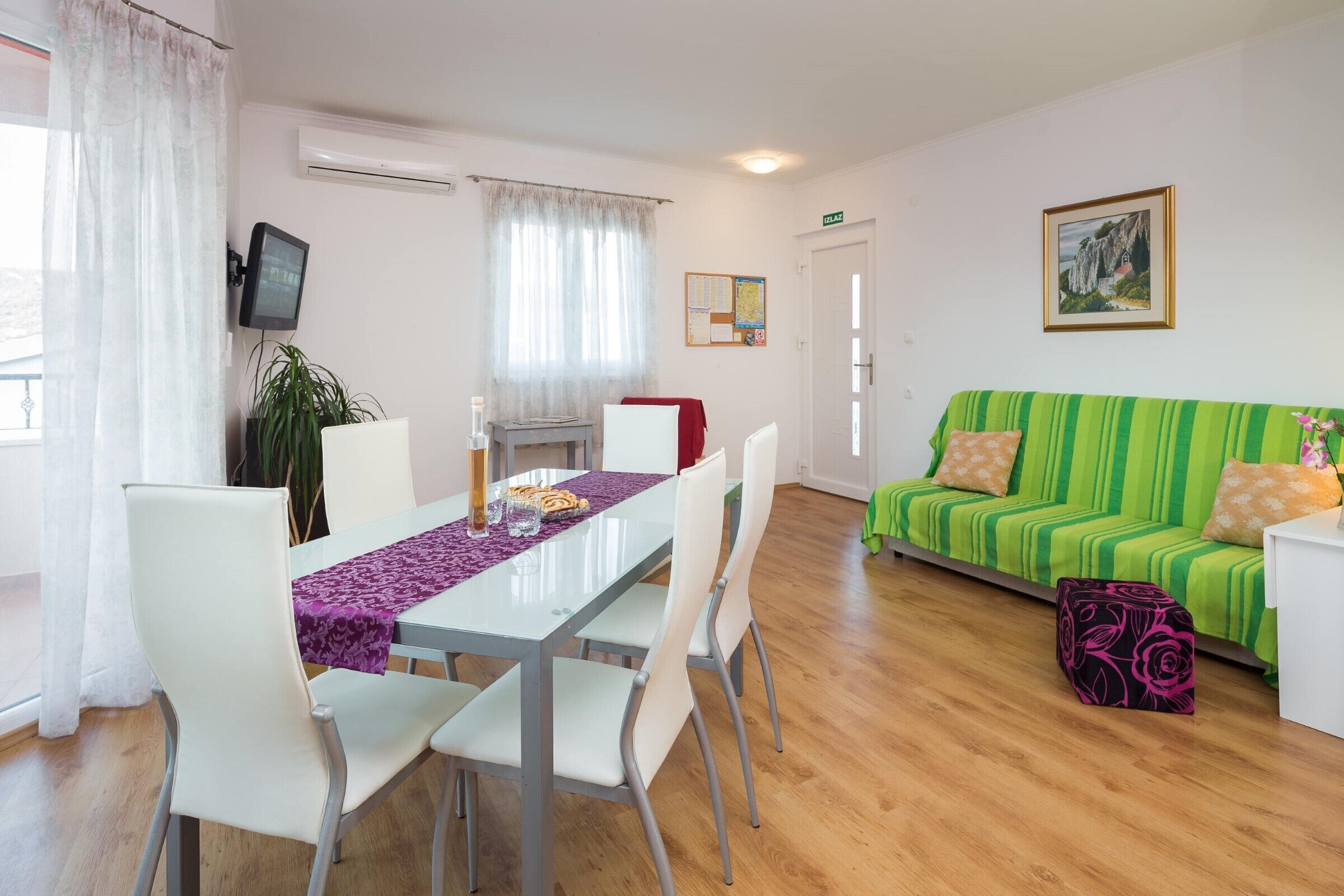 Ein modernes Wohnzimmer mit einem grün gestreiften Sofa, einem Esstisch mit weißen Stühlen und einem kleinen Tisch mit roter Tischdecke.