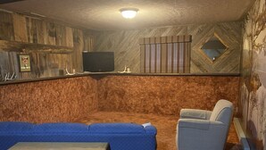 A room with a blue sofa, a grey armchair, a wooden table, a television mounted on a wooden wall, and a patterned wall. - 3 bedroom private vacation home in sundance (Sundance)