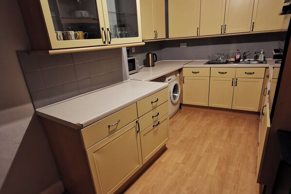 Una cocina compacta con armarios color beige, lavadora y microondas.