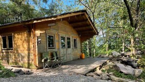 A rustic wooden cabin with a gravel driveway, a wooden deck, and a chair outside.