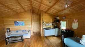 A cozy cabin interior with a wooden ceiling, a sofa, a dining table, and a kitchenette.