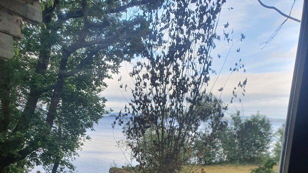 A view from a window overlooking a rocky shoreline with two green folding chairs on a wooden deck.