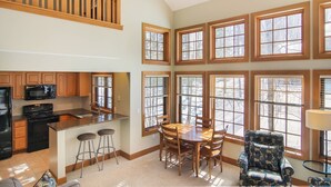 A spacious kitchen with wooden cabinets, a black stove, and a bar area with stools. - Disciples Village beautiful Condo - Steps to ski and lakes (Boyne Falls)