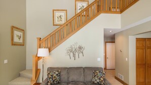 A living room with a grey sofa, a wooden staircase, and framed wall art. - Disciples Village beautiful Condo - Steps to ski and lakes (Boyne Falls)