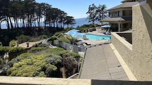 Un espace piscine offrant une vue sur l’océan, entouré d’arbres et bordé d’un bâtiment dont le toit est recouvert de tuiles.