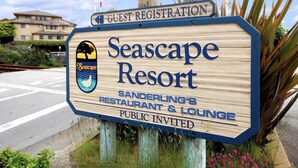 Une enseigne en bois indiquant le « Seascape Resort », avec un espace dédié à l’enregistrement des clients, et mentionnant le restaurant et le bar « Sanderling’s ».