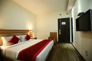 A hotel room with a bed, a nightstand, a TV mounted on the wall, and a door leading to another room. - PI Suites (New Delhi)