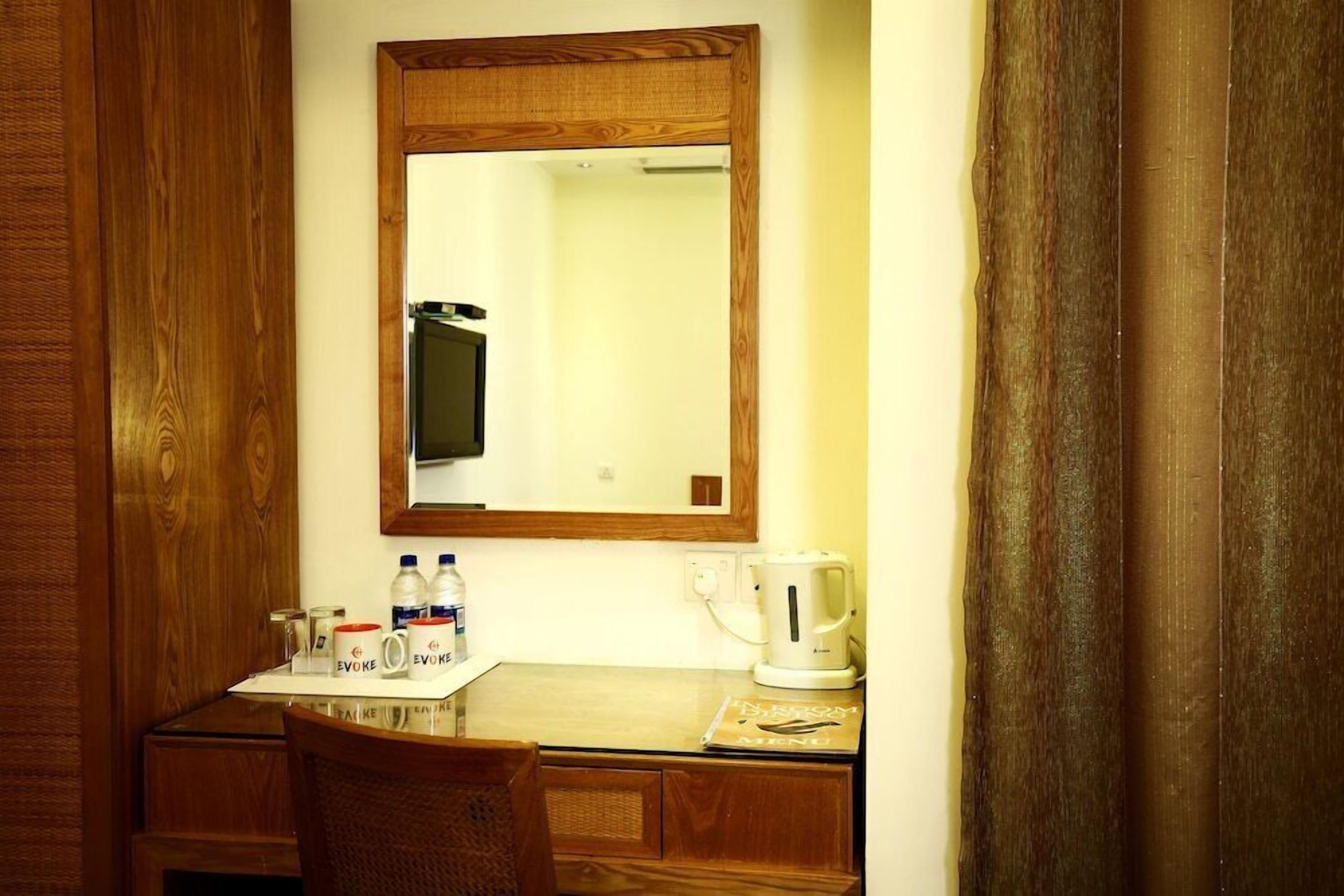 A small kitchenette with a wooden cabinet, a mirror, a coffee maker, and a table with a chair.