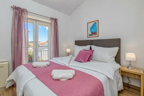 Uma cama bem arrumada com roupa de cama rosa e branca, um criado-mudo com abajur e um quadro na parede.