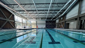 An indoor swimming pool with clear lanes, a tiled floor marked with '4 FT IN', and a high ceiling with visible structural beams.