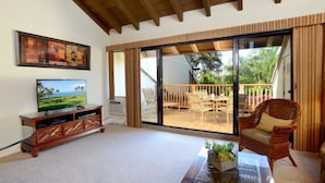 A spacious living area with a television, a glass coffee table, and a wicker chair. - Ocean-View Maui Kamaole Escape – A/C, Lanai, Walk to Beach & Pool! (Kihei)