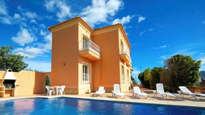 A poolside area with a clear blue pool, white lounge chairs, and a building with a balcony.