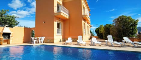 A poolside area with a clear blue pool, white lounge chairs, and a building with a balcony.