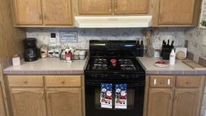 A kitchen with wooden cabinets, a stove, and a coffee maker. There is a sign on the wall that reads "COZY GETAWAY COTTAGE COFFEE HOUSE." - King size bedroom/ Outdoor fire pit, Game Room. Cozy getaway cottage (Cairo)