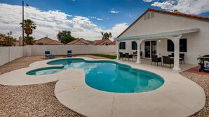 A swimming pool with a patio area, a covered outdoor seating area, and a white building with a red roof. - The Best House With A Heated Pool, Spa, and Safe, Sleeps 6 Comfortably (North Las Vegas)