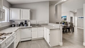 A modern kitchen with white cabinetry, a central island, and a dining area with a table and chairs. - The Best House With A Heated Pool, Spa, and Safe, Sleeps 6 Comfortably (North Las Vegas)