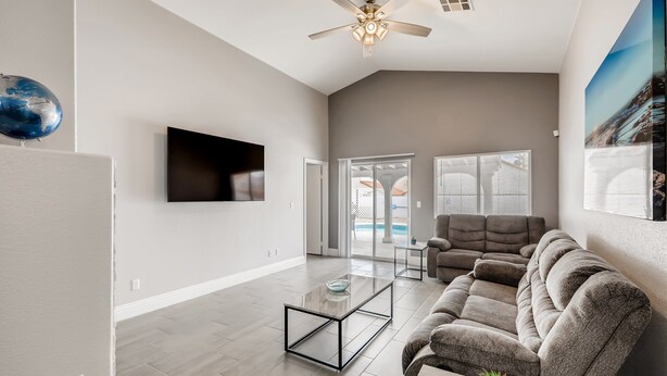 A spacious living room with a flat-screen TV, a ceiling fan, and a large window. - The Best House With A Heated Pool, Spa, and Safe, Sleeps 6 Comfortably (North Las Vegas)