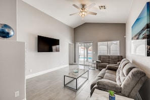 A spacious living room with a flat-screen TV, a ceiling fan, and a large window.