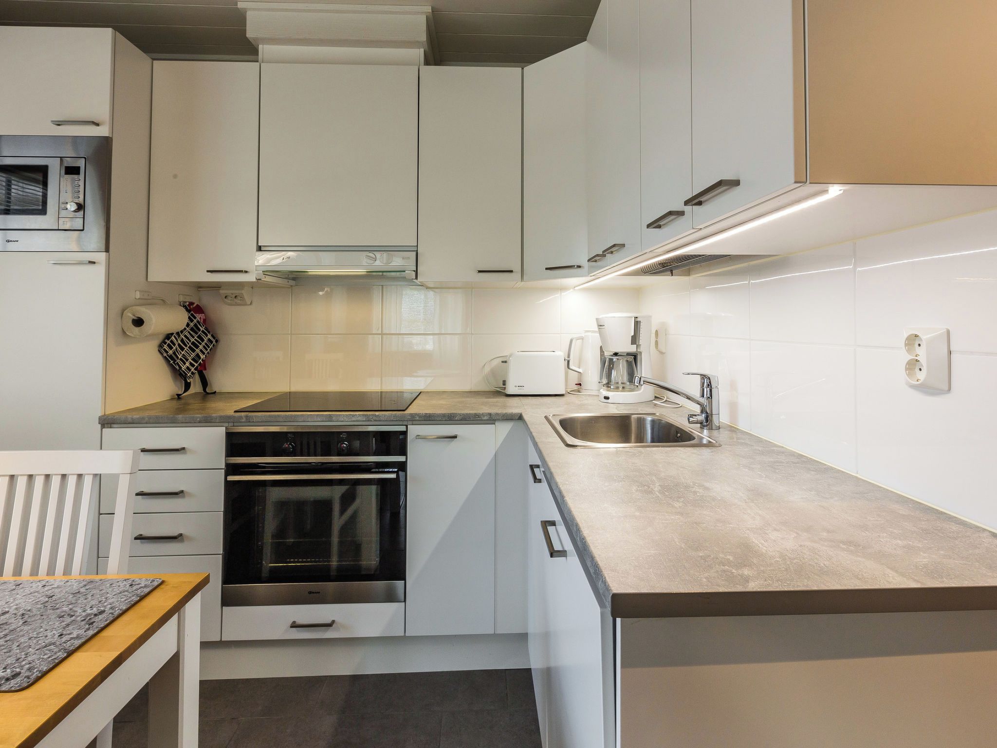 A modern kitchen with white cabinetry, a built-in oven, a stainless steel sink, and a coffee maker.