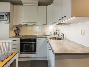 A modern kitchen with white cabinetry, a built-in oven, a stainless steel sink, and a coffee maker.