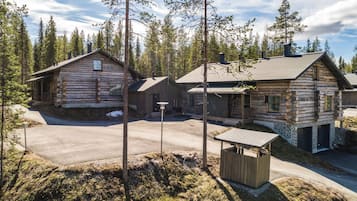 A log cabin with a porch, a stone structure, and a clear sky.