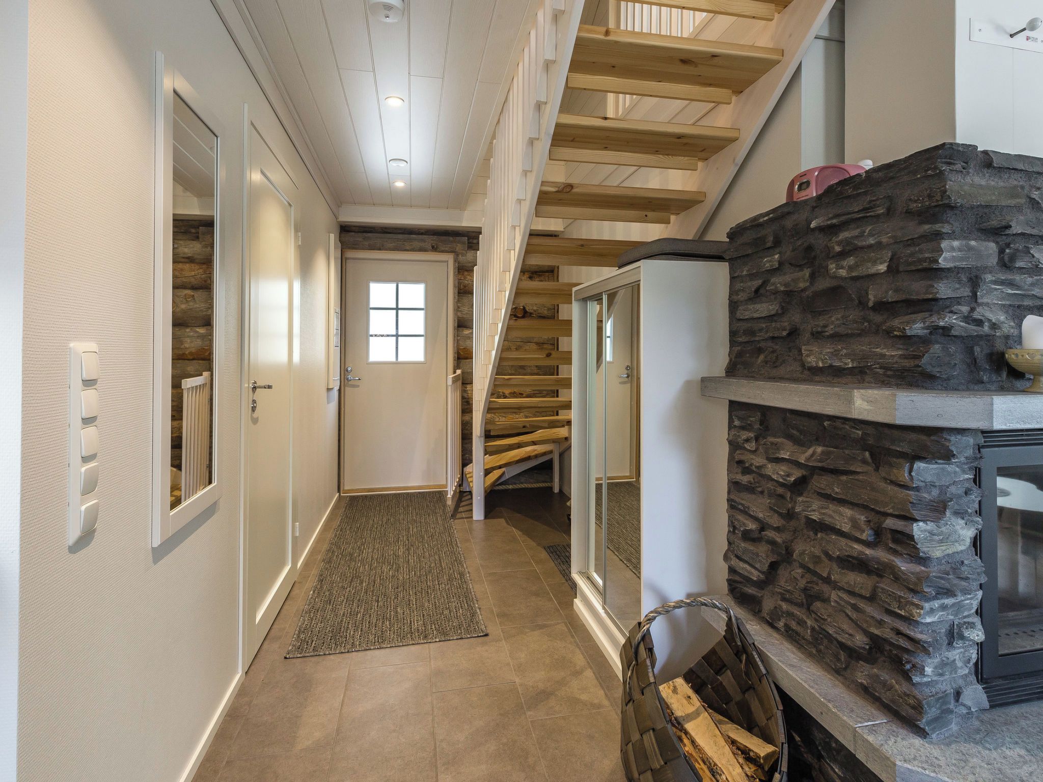 A hallway with a wooden staircase, a stone fireplace, and a door with a window.