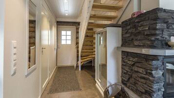 A hallway with a wooden staircase, a stone fireplace, and a door with a window.