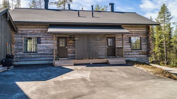 A log cabin with a covered porch, a driveway, and a forested backdrop.