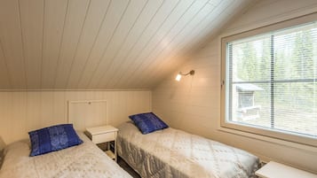 A bedroom with two beds, a nightstand, a window with blinds, and a sloped ceiling.