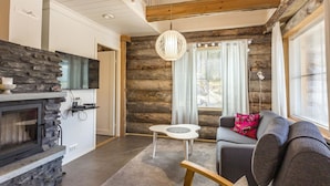 Ein gemütliches Blockhaus-Interieur mit Kamin aus Stein, einem grauen Sofa und einer Holzbalkendecke.