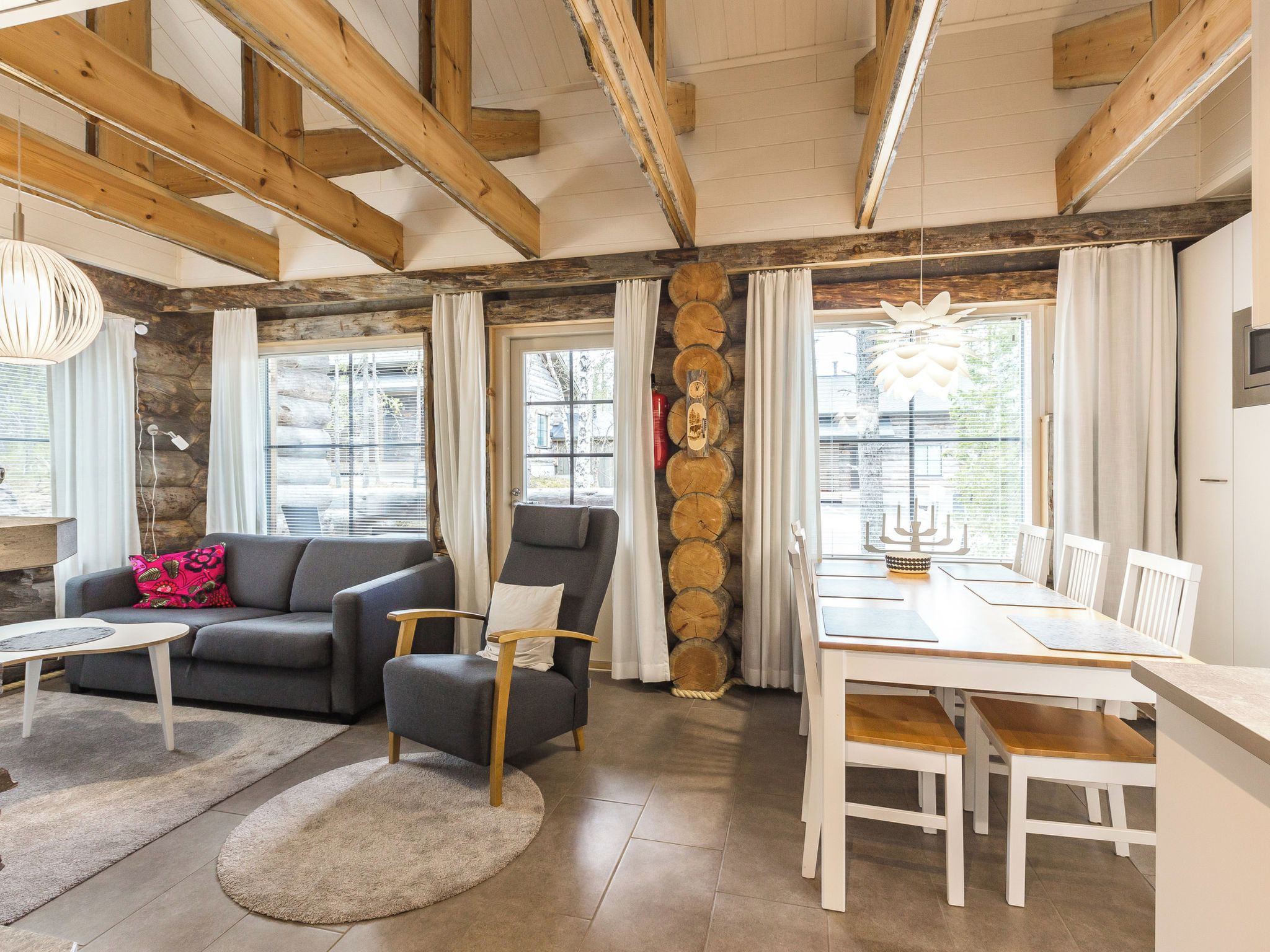 A modern living space with a sofa, armchair, dining table, and a fireplace with logs.