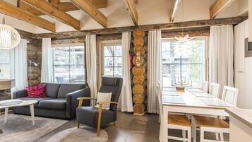 A modern living space with a sofa, armchair, dining table, and a fireplace with logs.