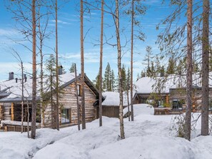Uma cabana de toras cercada por árvores altas e coberta de neve.