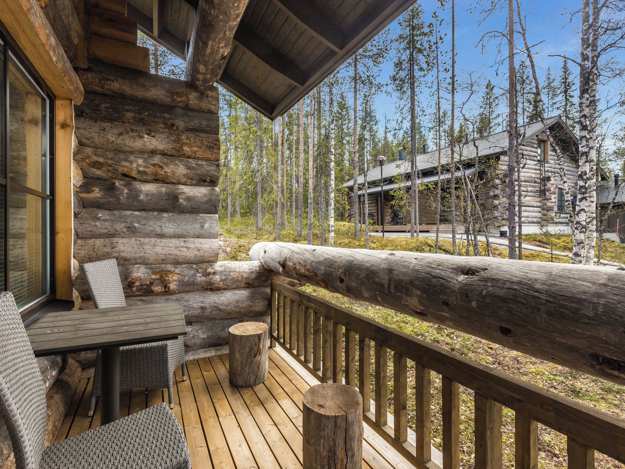 A log cabin with a deck, outdoor furniture, and a view of the surrounding forest.