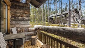 A log cabin with a deck, outdoor furniture, and a view of the surrounding forest.