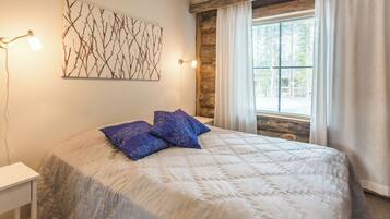 A bedroom with a bed, a nightstand, a wall-mounted light, a window with curtains, and a wooden log wall.
