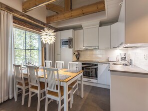 Una cocina moderna con armarios blancos, una mesa de comedor con sillas y un amplio ventanal con cortinas.