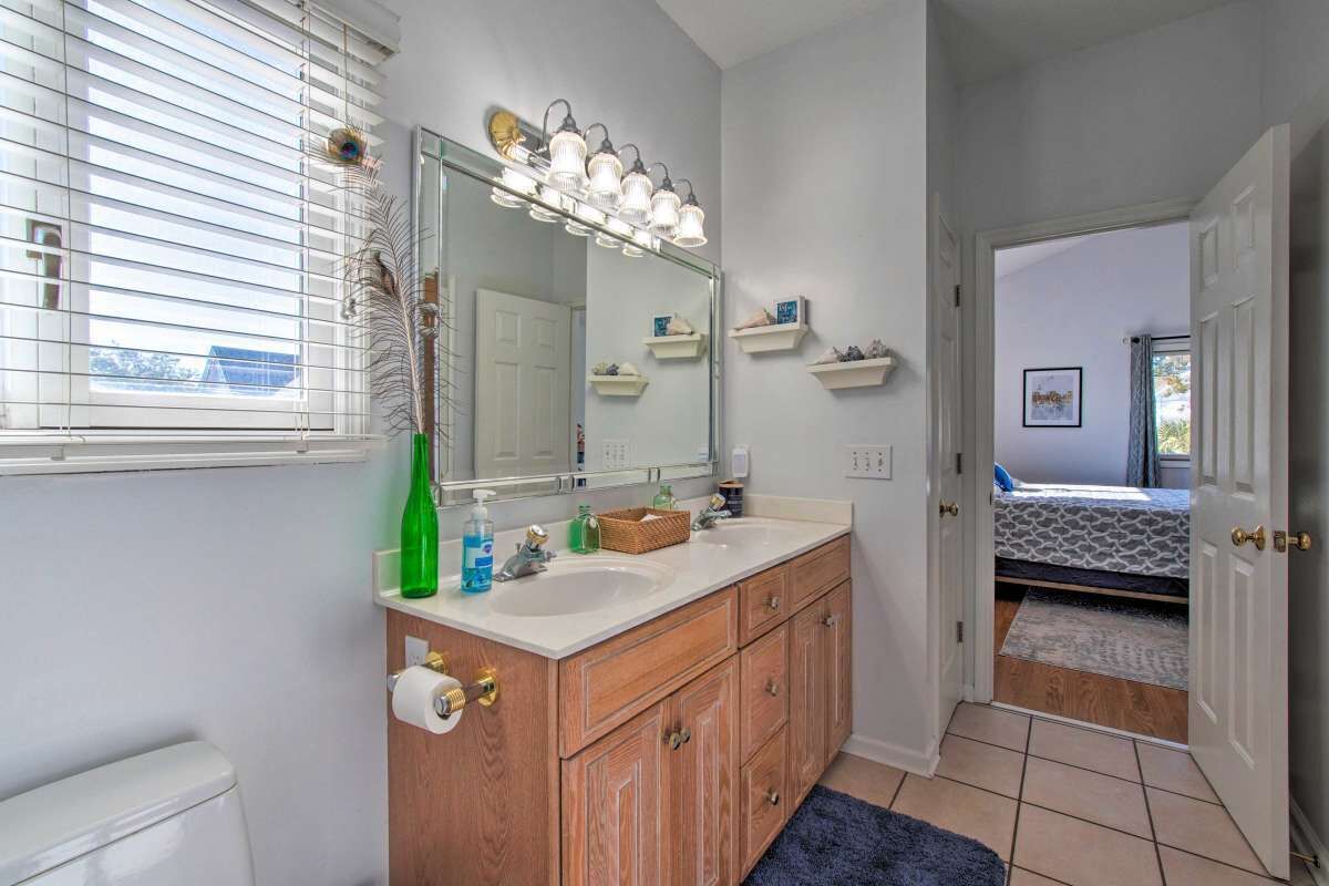 Une salle de bain avec un meuble-lavabo en bois, deux vasques, un grand miroir et une fenêtre avec des stores.