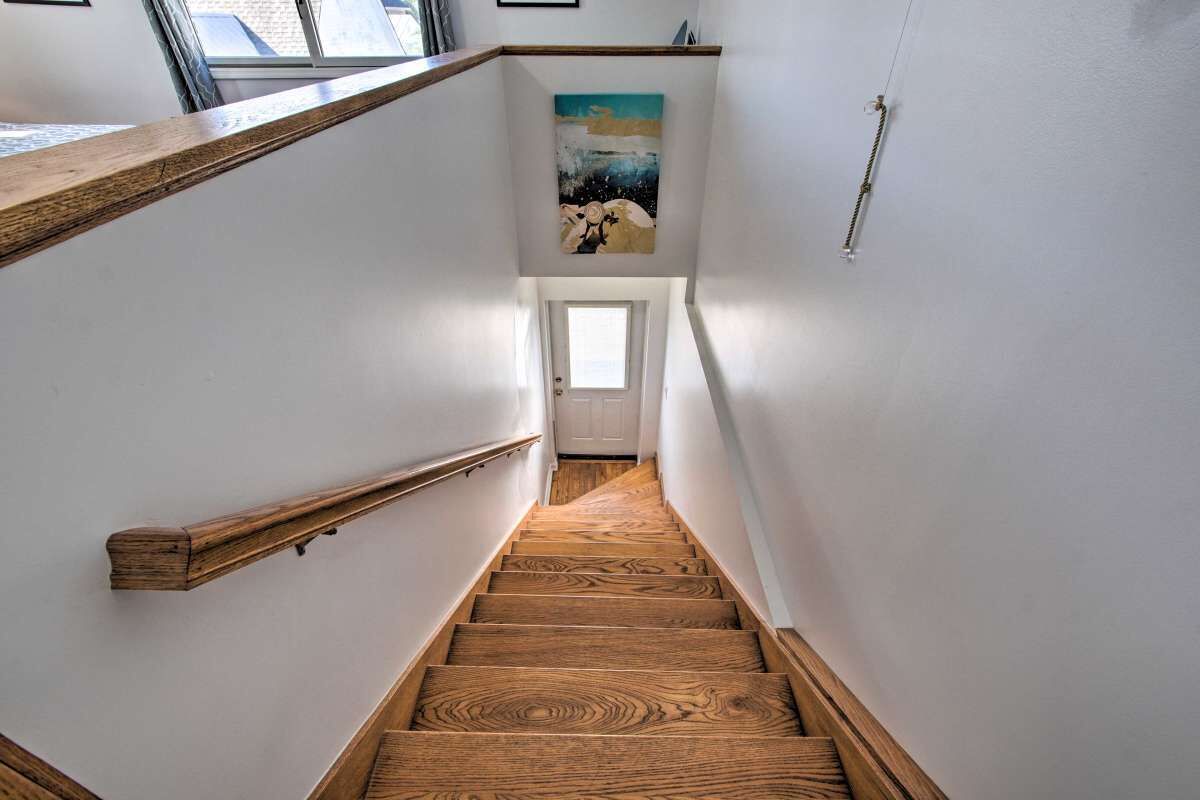 A wooden staircase with a handrail, white walls, and a painting above the door.