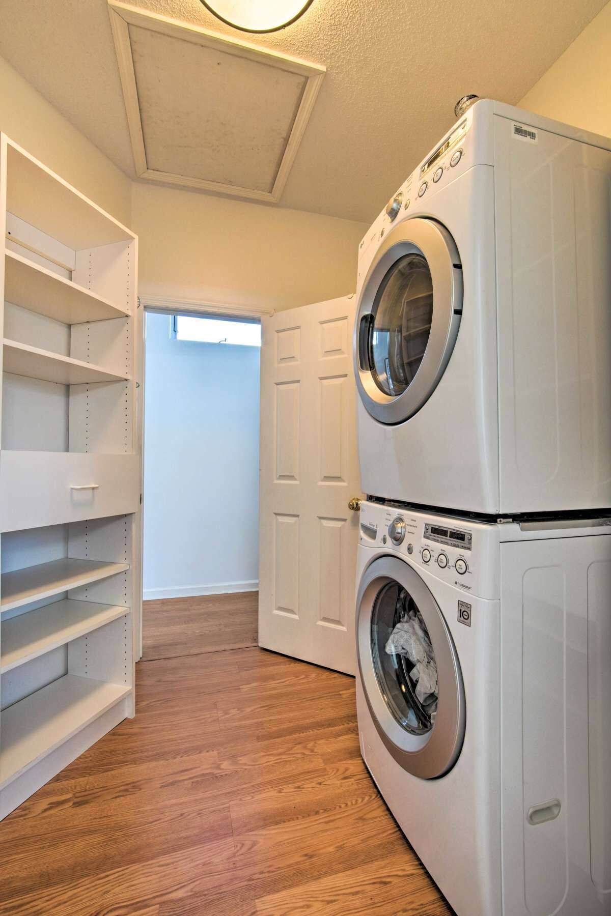 A laundry room with a double washer and dryer, wooden flooring, and a white shelving unit.