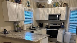 A kitchen with white cabinets, a central island with stools, a microwave, stove, and a sink. - 3 Bedroom house in Purple Parrot (Pensacola)