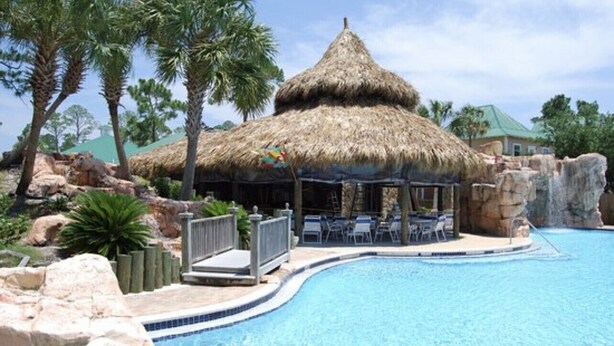 A pool area with a thatched-roof structure, palm trees, and a rocky landscape. - 3 Bedroom house in Purple Parrot (Pensacola)