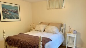 Une chambre à coucher avec un lit, une table de chevet, une lampe, un tableau au mur et une fenêtre avec des rideaux.