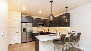 A modern kitchen with dark cabinets, a stainless steel refrigerator, a microwave, and a large island with bar stools. - Clearwater Lofts #104 Building 3 by Summit County Mountain Retreats (Keystone)