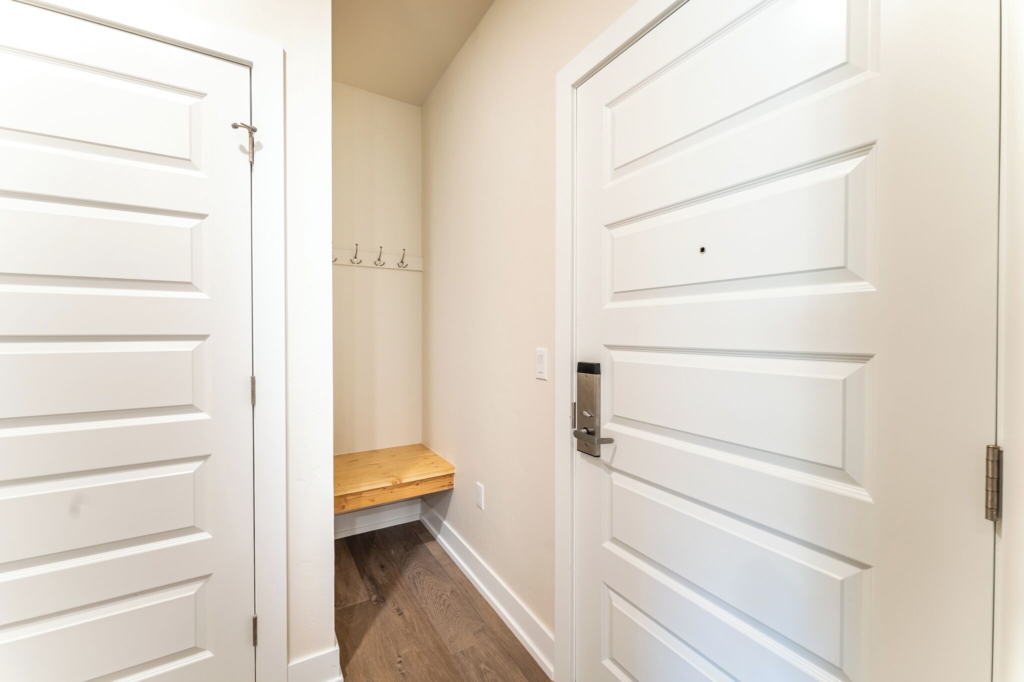 A hallway with two white doors, a wooden bench, and a coat rack.