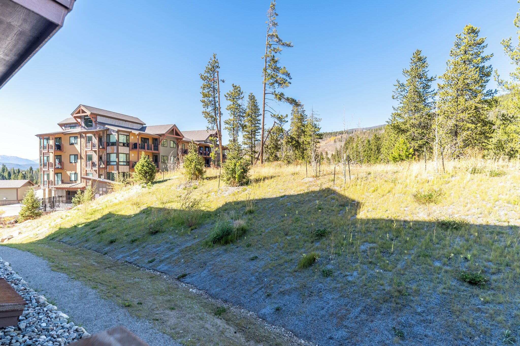 A multi-story building with a modern design, surrounded by a natural landscape with trees and a grassy slope.